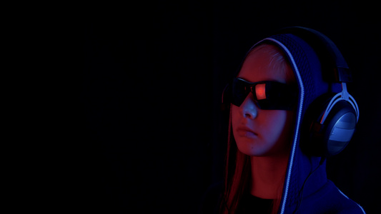 戴头套和耳机的少女在霓虹红和蓝色灯光的黑色工作室里视频
