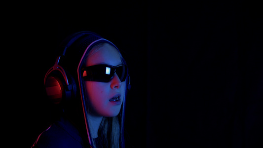 戴兜帽和黑色太阳镜的少女在黑暗的房间里用红色和蓝色视频