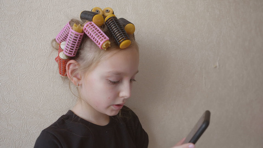 在轻墙背景使用智能手机的头发上卷发的少女女孩视频