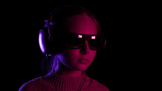 在红色和蓝色灯光的黑暗工作室里十几岁的女孩戴着耳机视频