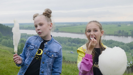 两个十几岁的女孩在夏季森林和河流景观上吃甜棉花用甜视频