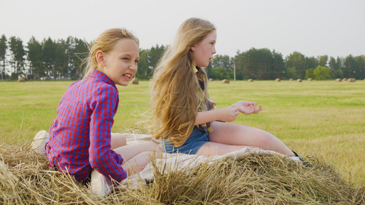 两个十几岁的女孩坐在农田农村田地的干草堆上快乐的女孩视频