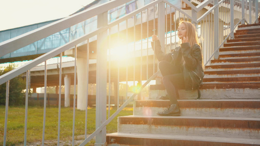 穿着黑色皮夹克的少女坐在阳光背景上的楼梯上穿着皮夹克视频