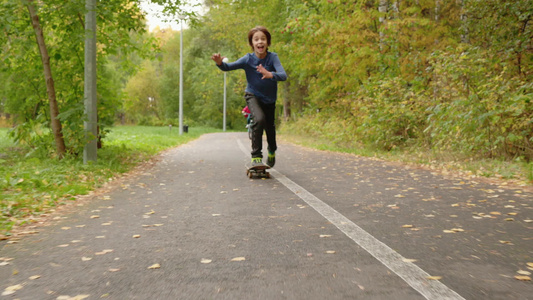 十几岁的男孩在公园小路上骑着滑板小男孩在秋季公园骑视频