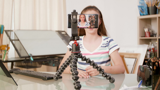智能手机在三脚架上拍摄一个年轻女孩说话视频