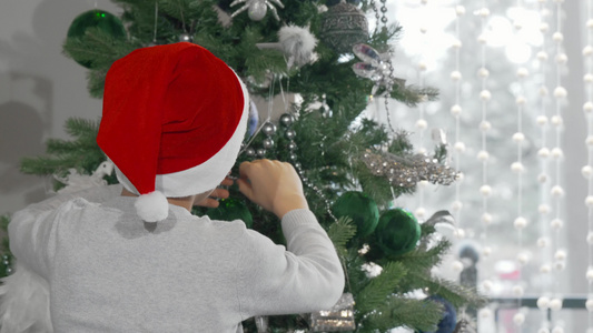 可爱的男孩在圣达克拉斯帽子装饰圣诞树视频