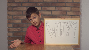 孩子坐在桌子上拿着翻页图写着为什么在红砖墙的背面6秒视频