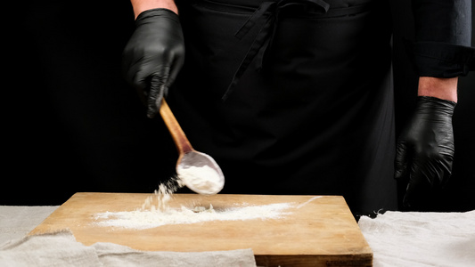 穿黑色制服和黑乳胶的厨师手套持有一勺配白面粉的木勺子视频