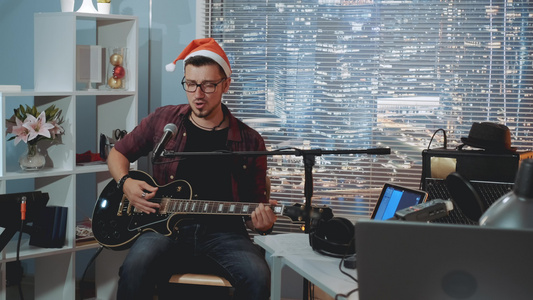 家庭录音演播室年轻的圣塔帽歌手在麦克风和吉他中唱圣诞歌视频