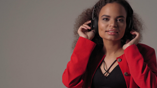 年轻快乐的非洲美国女孩在耳机里听音乐穿着红色夹克黑色视频