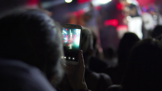 女孩手用相机手机在现场音乐会上拍照和录像智能手机记录视频