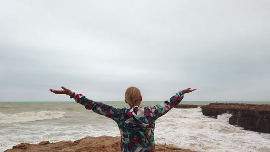 女孩举起手来在暴风雨中与她一起站在海岸上视频