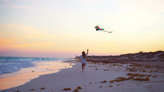 日落时在热带海滩上放风筝的小跑步女孩孩子们在海边玩耍视频
