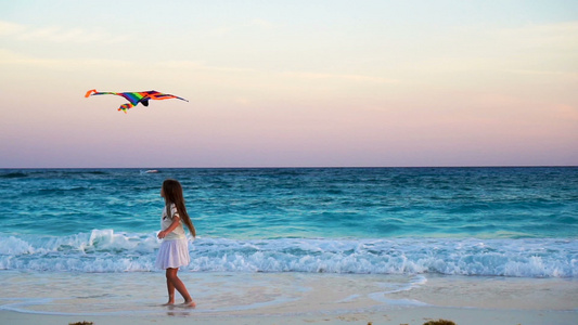 可爱的小女孩在热带海滩上放风筝孩子在海边玩日落美景视频