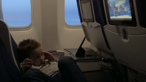 小男孩在飞机上靠着飞机窗的座位上戴着耳机看电影26秒视频