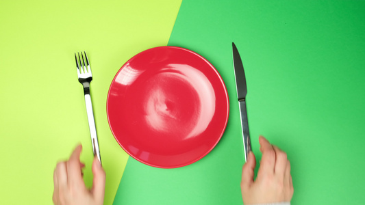 女用手放在绿色背景金属叉和刀子上紧靠一个空的红圆陶瓷视频