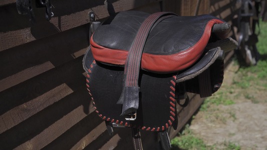 黑色和红色条纹皮革手工制作的马鞍挂在摊位附近的木托盘视频