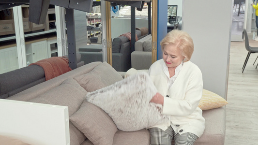快乐的老年妇女在家具店为自己的客厅选择坐垫并视频