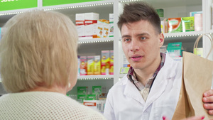 英俊的年轻药剂师向客户提供购物袋和购买10秒视频