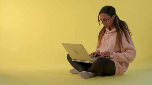 精明的非洲女孩在黄色背景上从事计算机工作视频