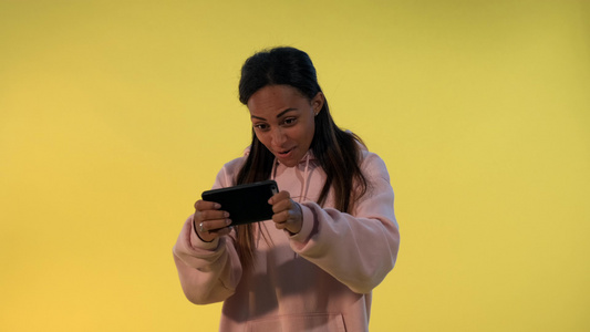 漂亮漂亮的黑人女孩在黄色背景的智能手机上玩游戏笑声视频