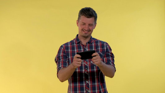 享受在黄色背景的智能手机上玩网上游戏的年轻男子积极视频