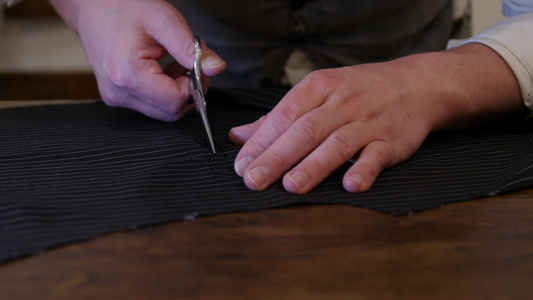 中年男子设计师手握剪刀在传统裁缝店工作室的桌面上剪视频