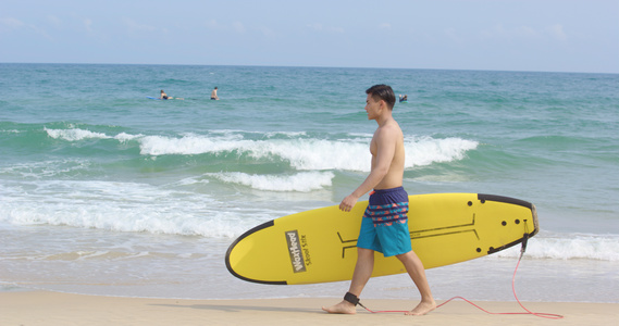8K海边男青年抱着冲浪板走在沙滩上视频