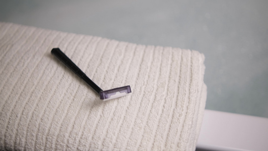 一个男人的手将一次性剃须刀放在浴室的毛巾上。一把黑色剃须刀。一条白毛巾。模糊的背景视频