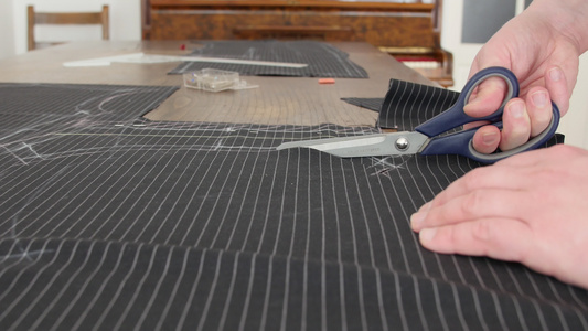 剪刀剪裁深灰色/黑色定制西装面料特写，这位男裁缝正在剪裁布料图案，用于定制夹克和裤子。创造时尚的过程视频