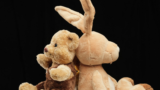 长耳朵兔子和多头泰迪熊在黑色背景下旋转,孩子们玩玩具视频