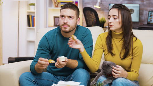 坐在沙发上吃炸鸡的年轻夫妇集中在一起视频