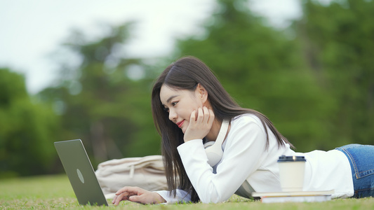 年轻女孩趴在草地上开心用电脑视频