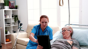 躺在床上的老年妇女向女医生学习如何使用平板电脑15秒视频