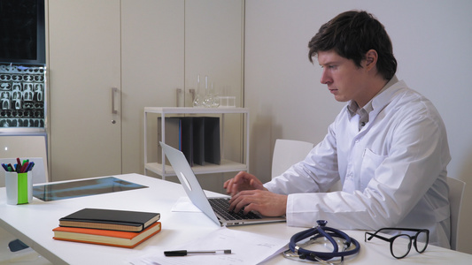 英俊的caucasian治疗师在办公室用笔记本电脑视频