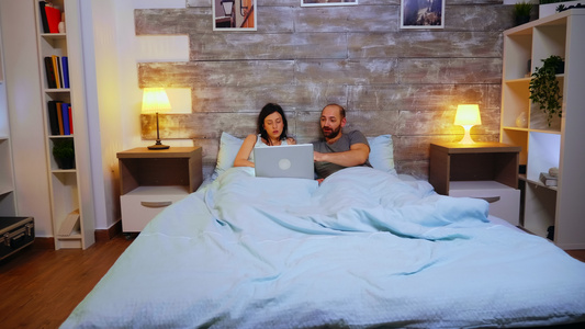 用笔记本电脑放大一对躺在毯子下床上的夫妇视频