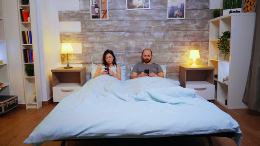 一对夫妇躺在舒适的床上用智能手机监听录音时放大镜头视频