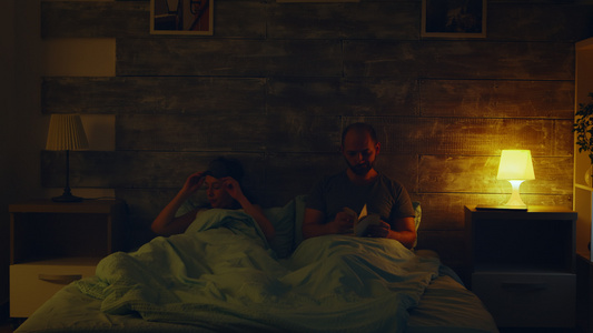 年轻男人在读一本书而他的妻子正在把灯关着睡觉视频