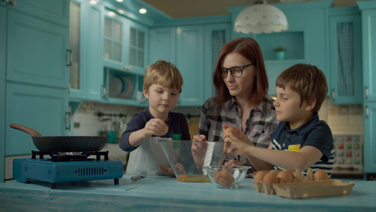 母亲和两个儿子在家里的蓝色厨房里一起煮炒鸡蛋的幸福家庭视频