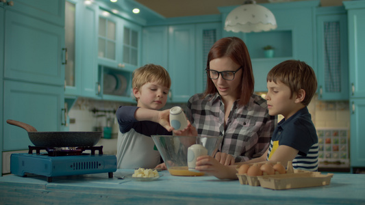 母亲和两个儿子在家里的蓝色厨房里一起煮炒鸡蛋的幸福家庭视频