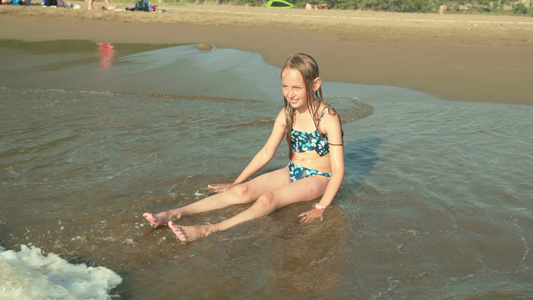 穿着泳装的可爱女孩坐在沙沙滩上享受海浪视频