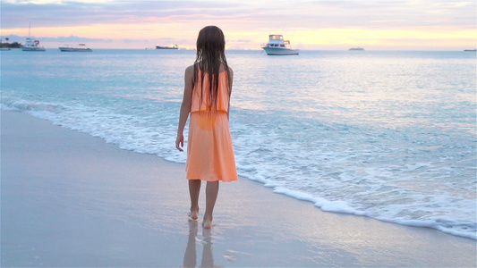 日落时在白沙滩上行走的可爱快乐小女孩慢动作视频