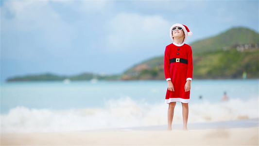 圣诞假期间在白沙滩上戴着圣诞帽的可爱小女孩视频
