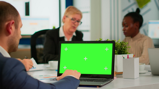 使用带绿色屏幕的笔记本电脑坐在会议桌的商务人员观看视频