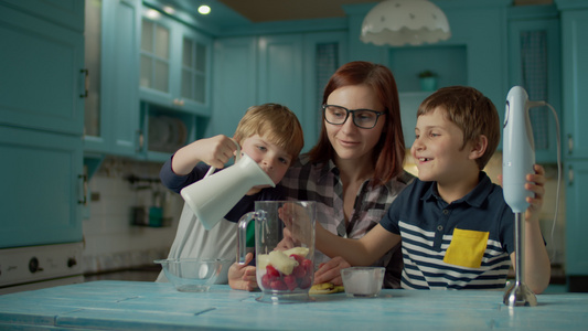幸福的母亲和两个孩子在家里的蓝色厨房里用搅拌机烹制视频