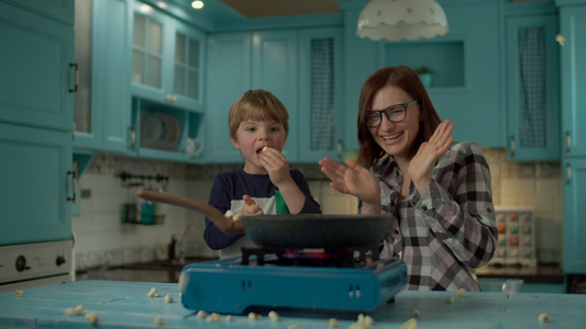 年轻的母子在家里蓝色厨房的煎锅上煮爆米花视频