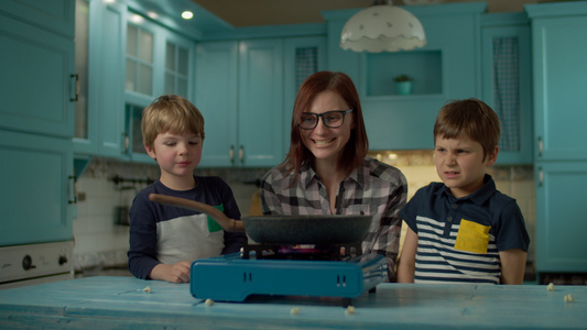 年轻母亲和两个儿子的幸福家庭在家里的蓝厨房做爆米花视频