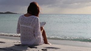 年轻女性坐在海边在黎明风中看着书本35秒视频