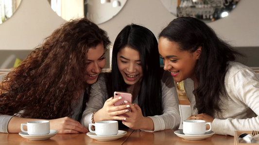 三个女孩在咖啡厅的智能手机上观看一些东西视频
