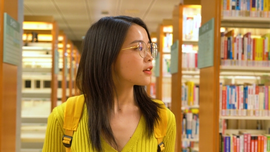 4k戴眼镜的女学生在图书馆里行走找书视频